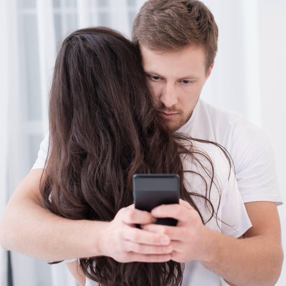 man-hugging-his-girlfriend-while-checking-his-phone